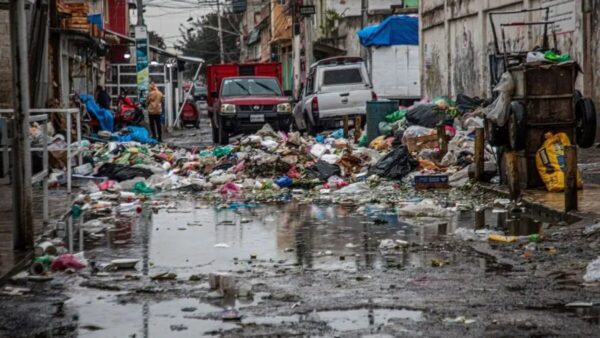 Vía urbana de la capital cubierta de desechos y charcos tras las lluvias, reflejo de los desafíos ambientales que contrastan con los discursos de sostenibilidad.