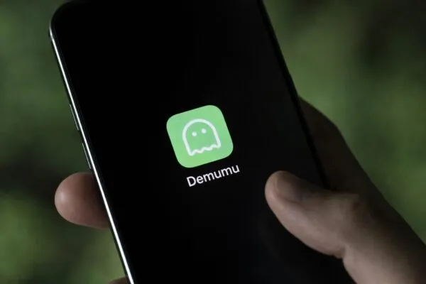 Teléfono mostrando Demumu app confirmando estado de vida con check-in diario