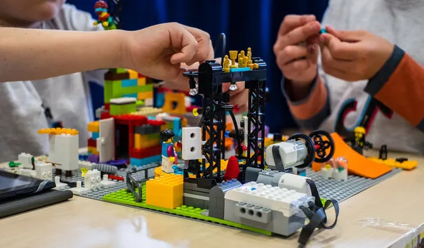 Robot construido con piezas LEGO junto a estructuras tecnológicas y elementos de programación educativa